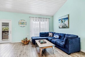 Ein Wohnzimmer mit einem blauen Sofa, einem Holztisch, einem runden Beistelltisch, einer Uhr und einem Gemälde an der Wand.