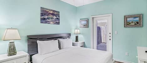A bedroom with a bed, a nightstand, a lamp, a ceiling fan, and a door leading to another room.