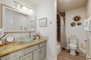 Un baño con lavamanos de vidrio, un espejo grande, un inodoro y detalles decorativos en la pared.
