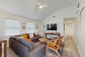 A living room with a sectional sofa, a coffee table, and a TV mounted on the wall. - Surf Inn - Under New Ownership (Port Aransas)