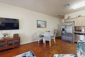 A compact living space with a dining area, a flat-screen TV mounted on the wall, a refrigerator, and a wooden cabinet. - Palm Bay 407 - Heated Pool & Covered Patio (Corpus Christi)