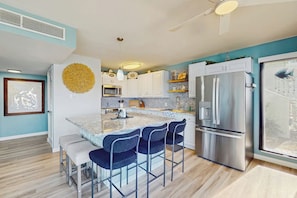 A modern kitchen with a central island, bar stools, stainless steel appliances, and a large window. - Puente Vista  120 - Wilson's Watering Hole - Captain’s Quarters (Corpus Christi)