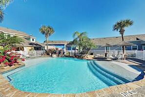 Ein Swimmingpool mit Steinbord, Palmen und einem weißen Zaun.
