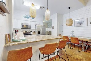 Eine moderne Küche mit weißen Schränken, einer Granit Arbeitsplatte und einer zentralen Kochinsel mit Barhocker.