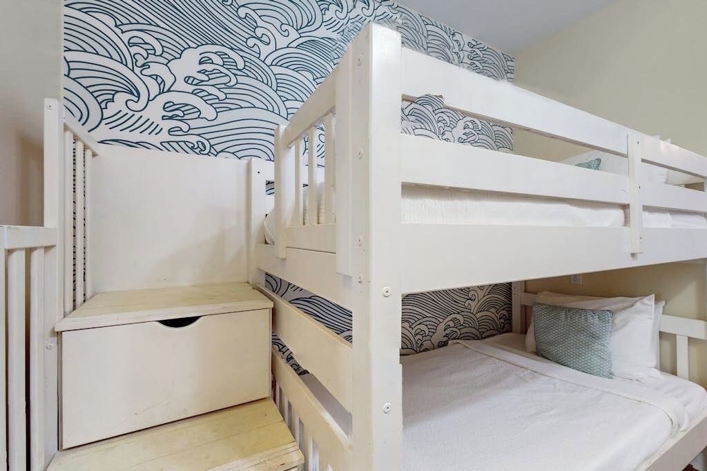 Un letto a castello con un letto inferiore e un cassetto contenitore, un comodino e una parete decorata.