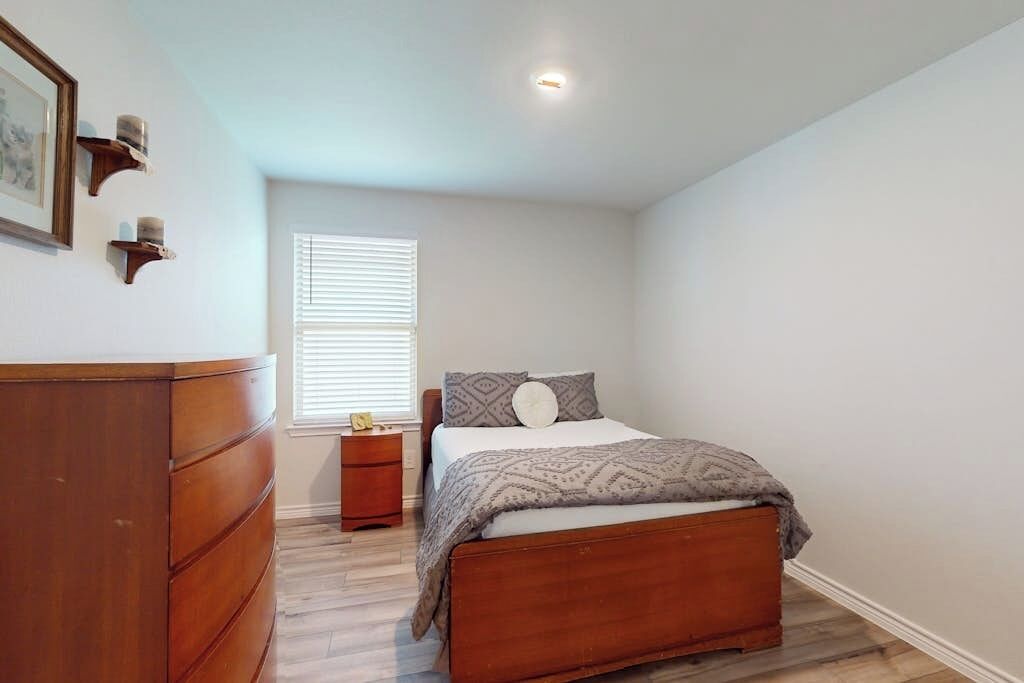Un dormitorio con una cama de madera, una mesita de noche, un tocador y una ventana con persianas.