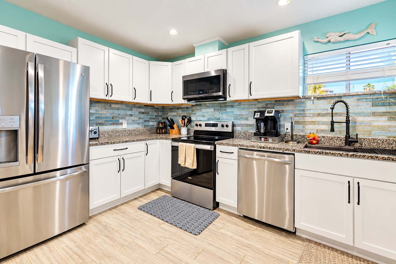 A modern kitchen with stainless steel appliances, white cabinetry, and a blue backsplash.