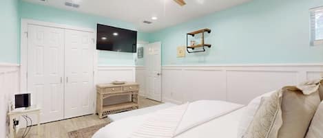 Un dormitorio con cama, ventilador de techo, televisor, cómoda y ventana.