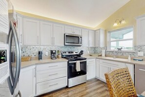 A kitchen with white cabinets, a stainless steel stove, a microwave, and a wicker chair. - The Lazy Bay - Canal-Front Home with Boat Dock (Rockport)