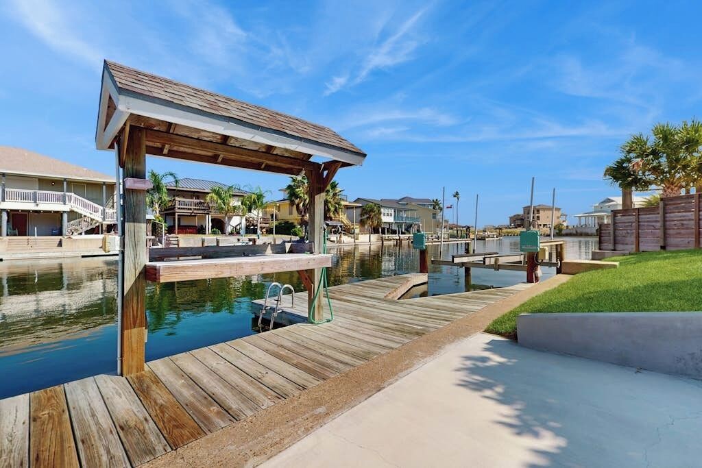 A waterfront property with a wooden dock, a covered seating area, and a pool.