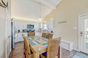 A kitchen with white cabinets, a microwave, and a dining area with a striped table and wicker chairs. - The Lazy Bay - Canal-Front Home with Boat Dock (Rockport)