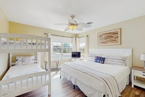 Une chambre avec un lit superposé, un lit simple, un ventilateur de plafond, une télévision et une fenêtre avec des rideaux.