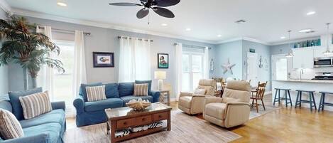 A spacious living room with a ceiling fan, a dining area with a kitchen in the background, and a large potted plant.