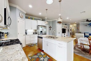 A kitchen with white cabinets, a central island, and a dining area with a table and chairs. - Fish Tail - Covered Patio & Yard, Near Beach (Rockport)