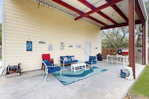 A covered patio with outdoor furniture, a flag, and a Texas state flag. - Fish Tail - Covered Patio & Yard, Near Beach (Rockport)