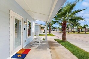 A covered porch with white rocking chairs, a palm tree, and a clear sky. - Kamp ENJoY #157 - Pool, Fishing Pond & Dogs OK (Rockport)