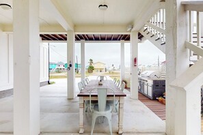 A covered outdoor dining area with a wooden table and metal chairs, a grill, and a view of the neighborhood. - A Sea Es La Vida - Water Views & Outdoor Kitchen (Rockport)