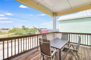 A wooden deck with a table and chairs, overlooking a view of a building and trees. - The Surf Rider, Unit 2 (Rockport)