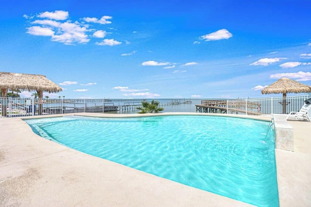 A clear blue swimming pool with a view of the ocean and a pier in the background.