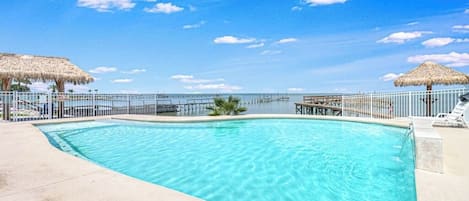 A clear blue swimming pool with a view of the ocean and a pier in the background.