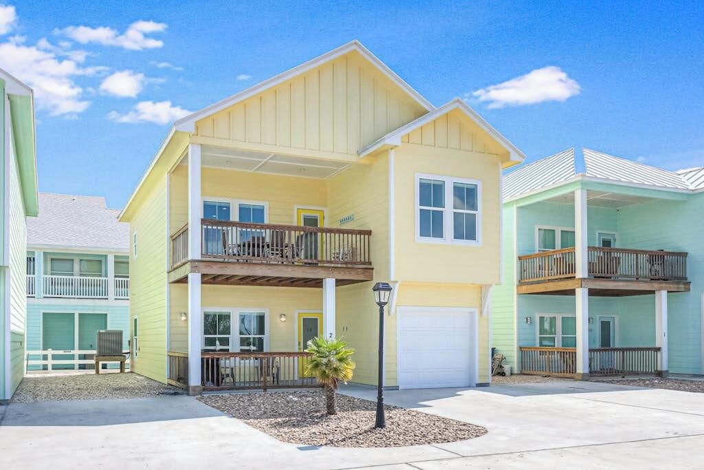 A two-story residential building with a balcony, a garage, and a small front yard with a palm tree.