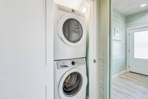 A laundry room with two stacked washing machines and a door leading to another room. - The Surf Rider, Unit 2 (Rockport)