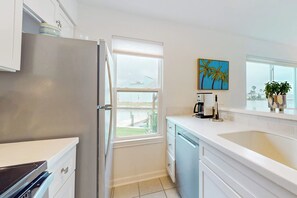 A modern kitchen with a refrigerator, dishwasher, and a window providing a view of the outdoors. - Pelican Point - Waterfront, Pool & Dock Access (Rockport)