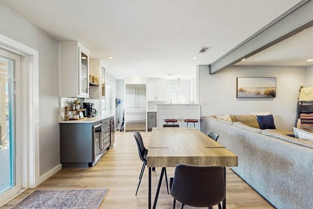 A modern kitchen with a dining area, a sofa, and a view of the outdoors.