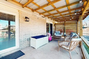 A covered outdoor area with a pool, wicker furniture, and a white storage unit. - The Bluff Breeze - Canal-Front with Large Yard (Corpus Christi)