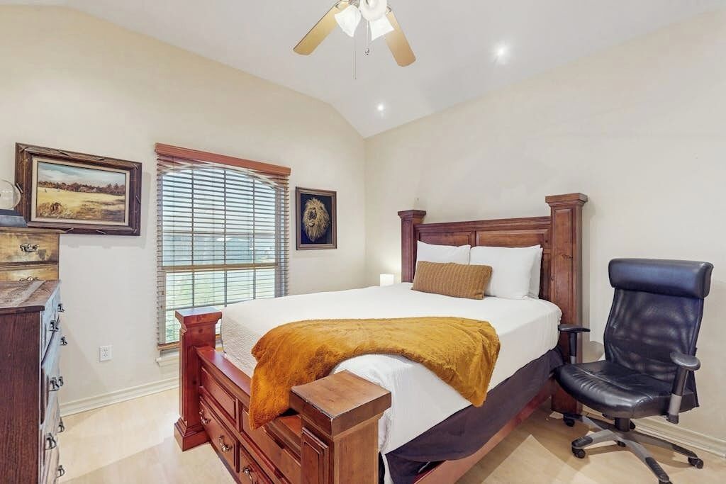 Un dormitorio con una cama, un escritorio, una silla, un ventilador de techo y una ventana con persianas.