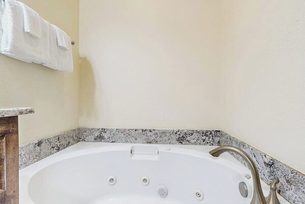 A bathroom with a white bathtub, a granite countertop, and a towel rack. - Ron's Retreat - Steps to Sand, Yard & Dogs OK (Corpus Christi)