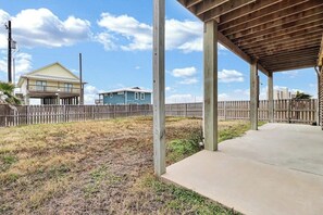 A covered outdoor area with a concrete floor, wooden pillars, and a wooden fence in the background. - Blue Pelican - Bayfront, Fenced Yard & Balconies (Corpus Christi)
