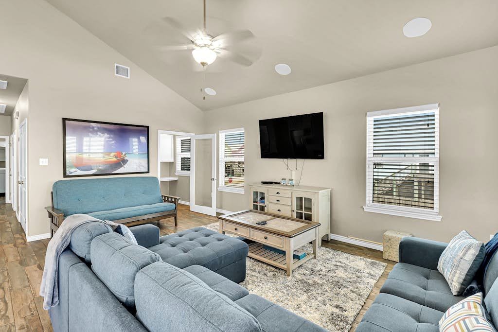 A living room with a sofa set, a coffee table, a flat-screen TV, and a ceiling fan.
