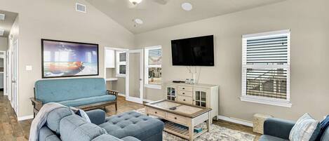 A living room with a sofa set, a coffee table, a flat-screen TV, and a ceiling fan.