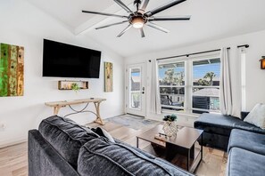 Ein modernes Wohnzimmer mit Flachbildfernseher, Deckenventilator und einem großen Fenster mit Blick nach draußen.