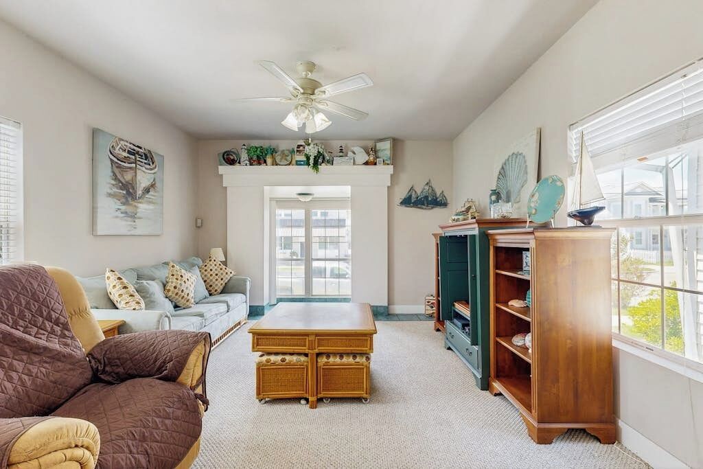 A living room with a sofa, a coffee table, a bookshelf, and a ceiling fan.