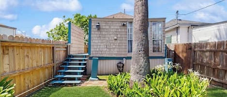 A residential backyard with a wooden fence, a staircase, a palm tree, and a small garden area.