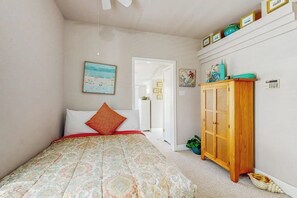 A bedroom with a bed, a wooden cabinet, and a door leading to another room. - Seashell Shack - Cozy Galveston Home, Fenced Yard (Galveston)