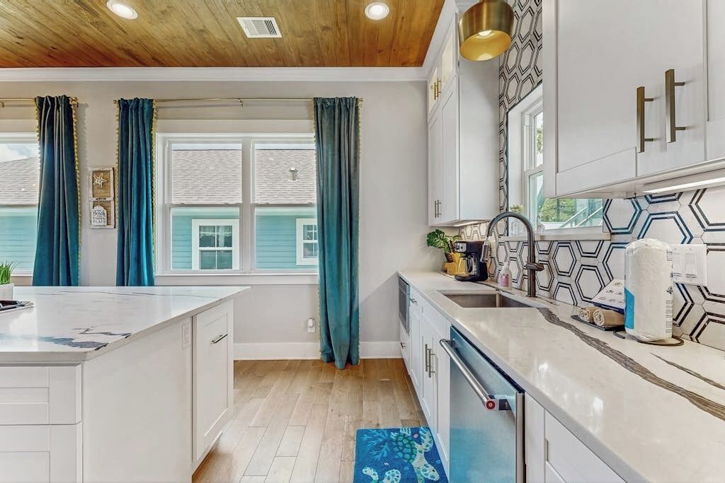 Une cuisine moderne avec des meubles blancs, un plan de travail en marbre et une fenêtre agrémentée de rideaux turquoise.