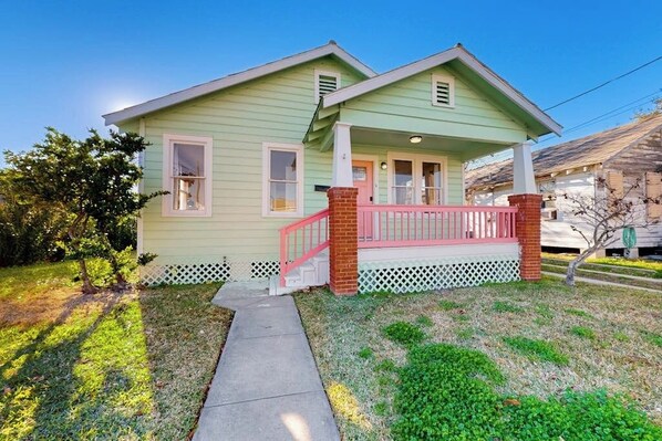 A two-story house with a front porch, a small front yard, and a visible staircase leading to the entrance. - Kay's Kottage - Fenced Yard, Near Beach & Seawall (Galveston)