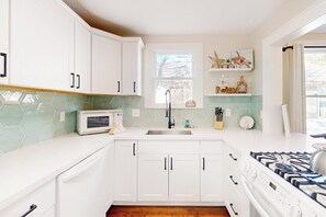 A kitchen with white cabinets, a microwave, a sink, and a gas stove. - Kay's Kottage - Fenced Yard, Near Beach & Seawall (Galveston)