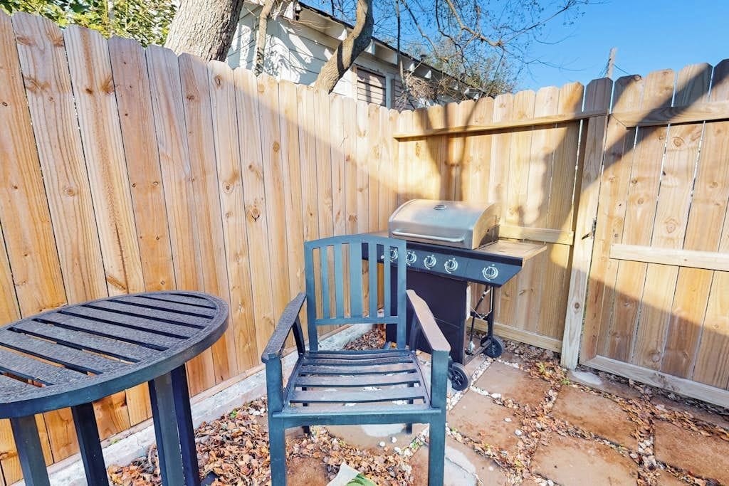 A wooden fence, a grill, and a chair in a backyard.