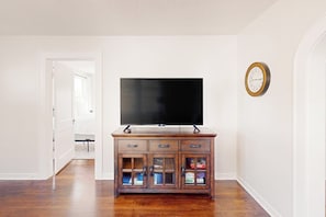 A room with a wooden cabinet, a flat-screen TV, and a wall clock. - Kay's Kottage - Fenced Yard, Near Beach & Seawall (Galveston)