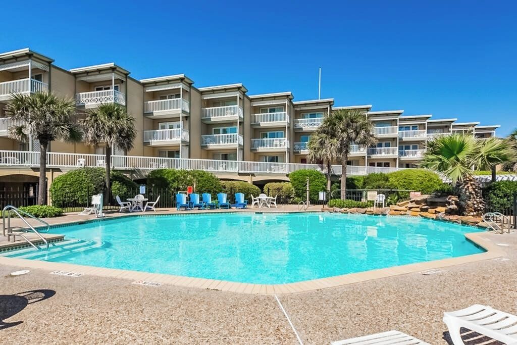 Une piscine avec des chaises longues et, au fond, un bâtiment doté de balcons.