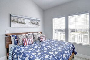 A bedroom with a bed, a headboard, a window with blinds, and a wall-mounted artwork. - Pathway to the Sea 14838 (Corpus Christi)