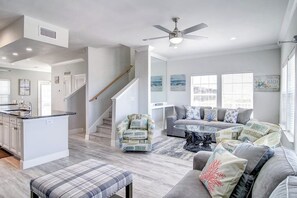 A spacious living area with a gray sofa, a coffee table, and a patterned armchair. A staircase with a wooden handrail leads to another level. - Pathway to the Sea 14838 (Corpus Christi)