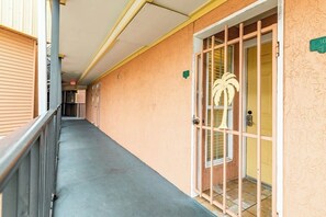 A corridor with a metal railing, a door with a palm tree decoration, and a number sign on the wall. - Victorian 7103 - Beachfront, Pools & Hot Tubs (Galveston)