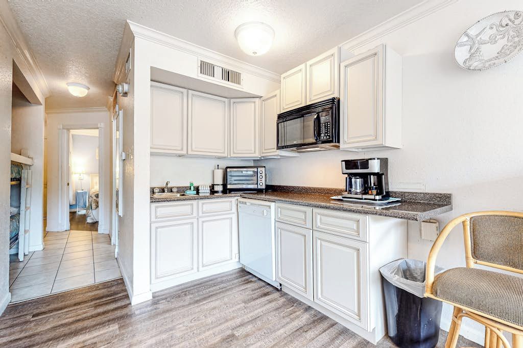 A kitchen with white cabinetry, a microwave, a coffee maker, and a trash can.