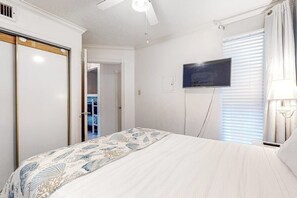 A bedroom with a bed, a television mounted on the wall, and a ceiling fan. - Victorian 7103 - Beachfront, Pools & Hot Tubs (Galveston)