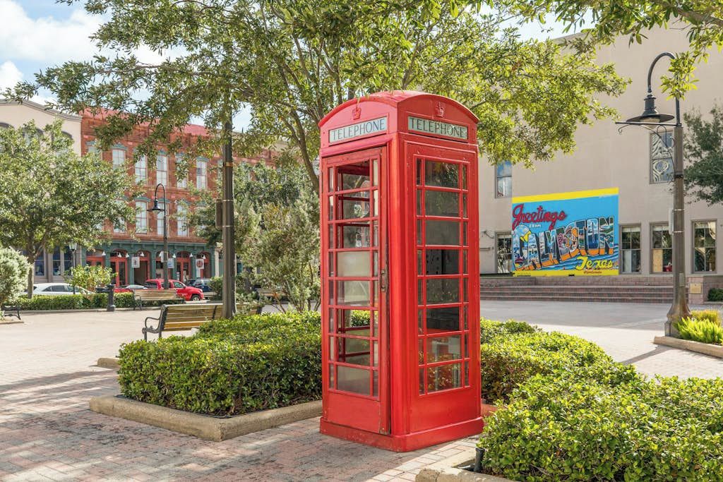 A red telephone booth in a public square with a mural in the background.